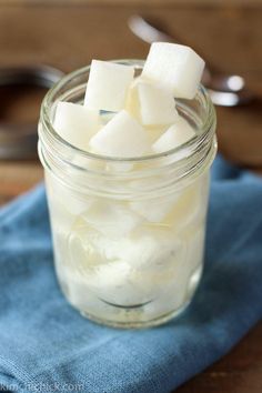 a glass jar filled with sugar cubes on top of a blue cloth next to spoon