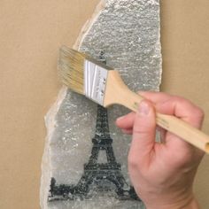 a hand holding a paintbrush over a piece of paper with the eiffel tower on it