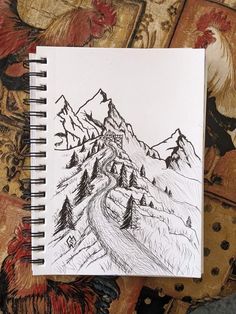 a notebook with a drawing of mountains and trees on the cover is sitting on a bed