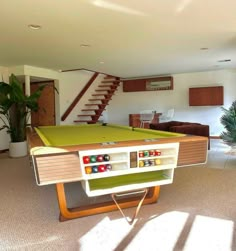 a pool table in the middle of a living room with stairs leading up to it