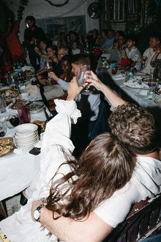 a group of people sitting at a table with wine glasses in their hands and plates on the ground