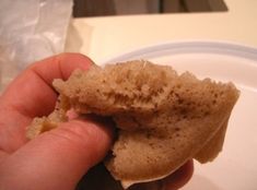 a hand holding a piece of bread over a white plate with plastic wrapper on it