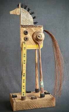 a wooden horse with long hair on it's head and measuring tape in its mouth