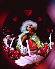 a woman with white hair is surrounded by candles and candies in the shape of hearts