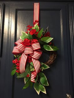 a wreath with red flowers and green leaves hanging on a door