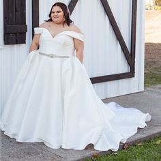 a woman in a white wedding dress standing next to a barn with her hands on her hips