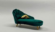 a small green chair with a gold pillow on it's back, sitting in front of a white background