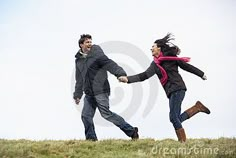 a man and woman holding hands while walking across a grass covered field with the sky in the background