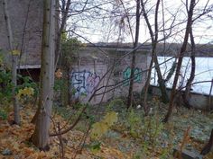 graffiti is spray painted on the side of an old brick wall near trees and water