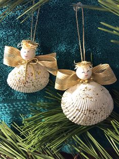 two christmas ornaments hanging from a pine branch on a blue cloth covered background with green needles