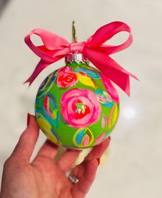 a hand holding a green ornament with pink flowers and a bow on it