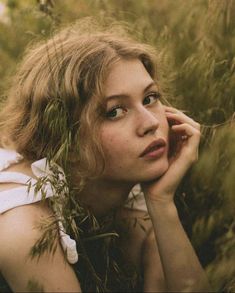 a woman laying in the grass with her hand on her chin and looking at the camera