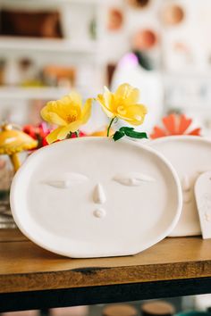 two white plates with faces on them sitting on top of a wooden table next to yellow flowers