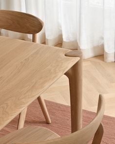 a wooden table with two chairs next to it in front of a curtained window