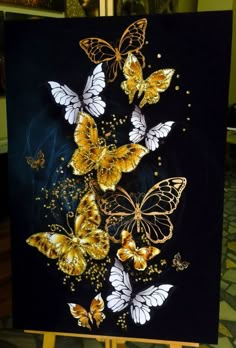 a painting with gold and white butterflies painted on it's black canvas, sitting on a easel