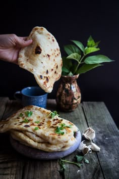 a hand is holding a pita bread over a plate with garlic and parsley