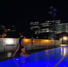 a woman sitting on the edge of a swimming pool at night