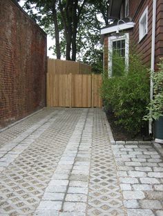 a brick walkway in front of a house with a wooden fence and trees on the other side