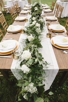 a long table with white flowers and greenery is set up for an outdoor dinner