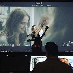 a woman standing in front of a large screen with her arms up and hands raised