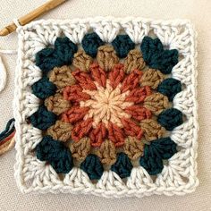 a crocheted square with an orange and blue flower on it next to a pair of scissors