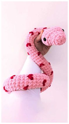 a hand holding a pink knitted snake with red hearts on it's tail