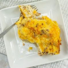 a white plate topped with an omelet covered in meat and cheese next to a fork