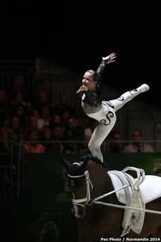 a woman riding on the back of a brown horse while holding her leg up in the air