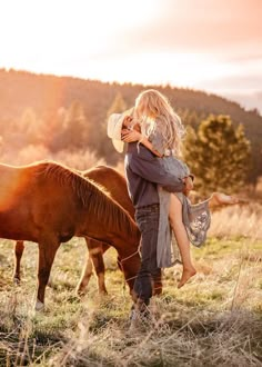 a man and woman hug while standing next to horses