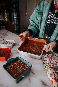 a woman holding a tray of chocolate cake next to other baking dishes on a table