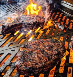 two steaks cooking on the grill with flames