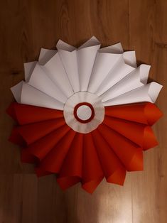 a red and white paper fan sitting on top of a wooden floor next to a wall