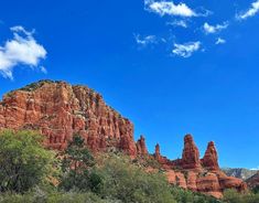 red rock formations with trees in the foreground and clouds in the sky above them