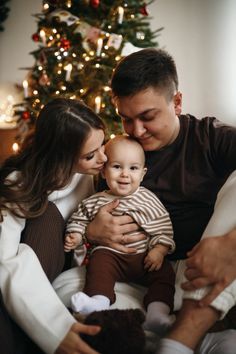 a man and woman holding a baby in front of a christmas tree