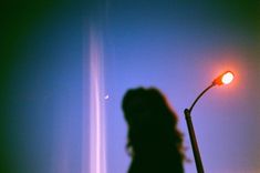 a woman standing next to a street light in the dark with her shadow on the wall