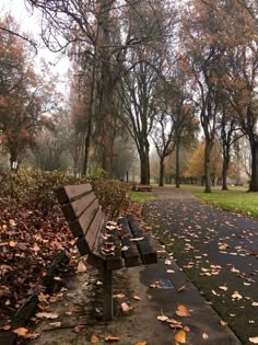 a park bench sitting on top of a sidewalk covered in leaves