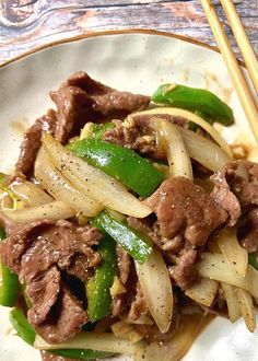 a white plate topped with meat and vegetables next to chopsticks on a table