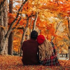 two people sitting on the ground in front of trees with leaves all around them and one person is holding his head back