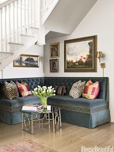 a blue couch sitting under a stair case next to a table with flowers on it