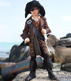 a young boy dressed in pirate costume standing on rocks