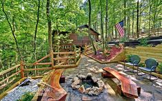 an outdoor fire pit in the middle of a wooded area with benches and chairs around it