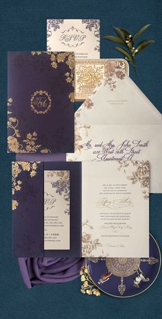 the wedding stationery is purple and gold, with an elegant floral design on it