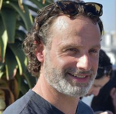 a close up of a person wearing sunglasses and smiling at the camera with other people in the background