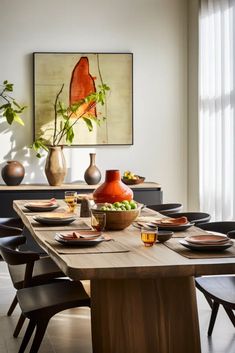 a dining room table with plates and bowls on it, in front of a painting