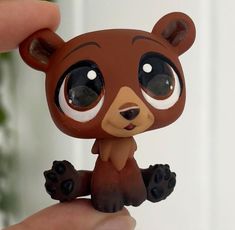 a little brown bear with big eyes sitting on someone's finger