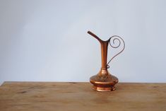 a small copper vase sitting on top of a wooden table