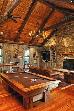 a pool table in the middle of a living room with wood floors and exposed ceiling