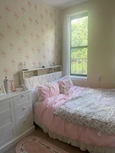 a bedroom with pink bedding and floral wallpaper, along with white dressers