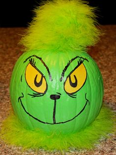 a green pumpkin with yellow eyes and a furry tail on the top, sitting on a counter