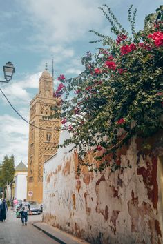 people walking down the street in front of a building with flowers growing out of it